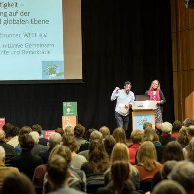 Nachhaltigkeitstagung 2018: Nachhaltigkeit first; zwei Referierende stehen vor Publikum auf der Bühne des Tagungssaals
