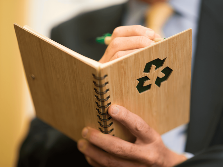 Mann notiert in ein Holzbuch mit Recycling-Logo