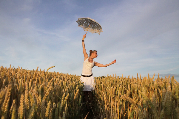 Eine tanzende Frau steht mit einem Sonnenschirm in der Hand in einem Getreidefeld