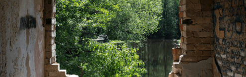 Blick durch einen Durchbruch in einem Rohbau ins Grüne und auf einen See