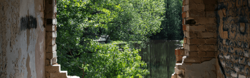 Blick durch einen Durchbruch in einem Rohbau ins Grüne und auf einen See